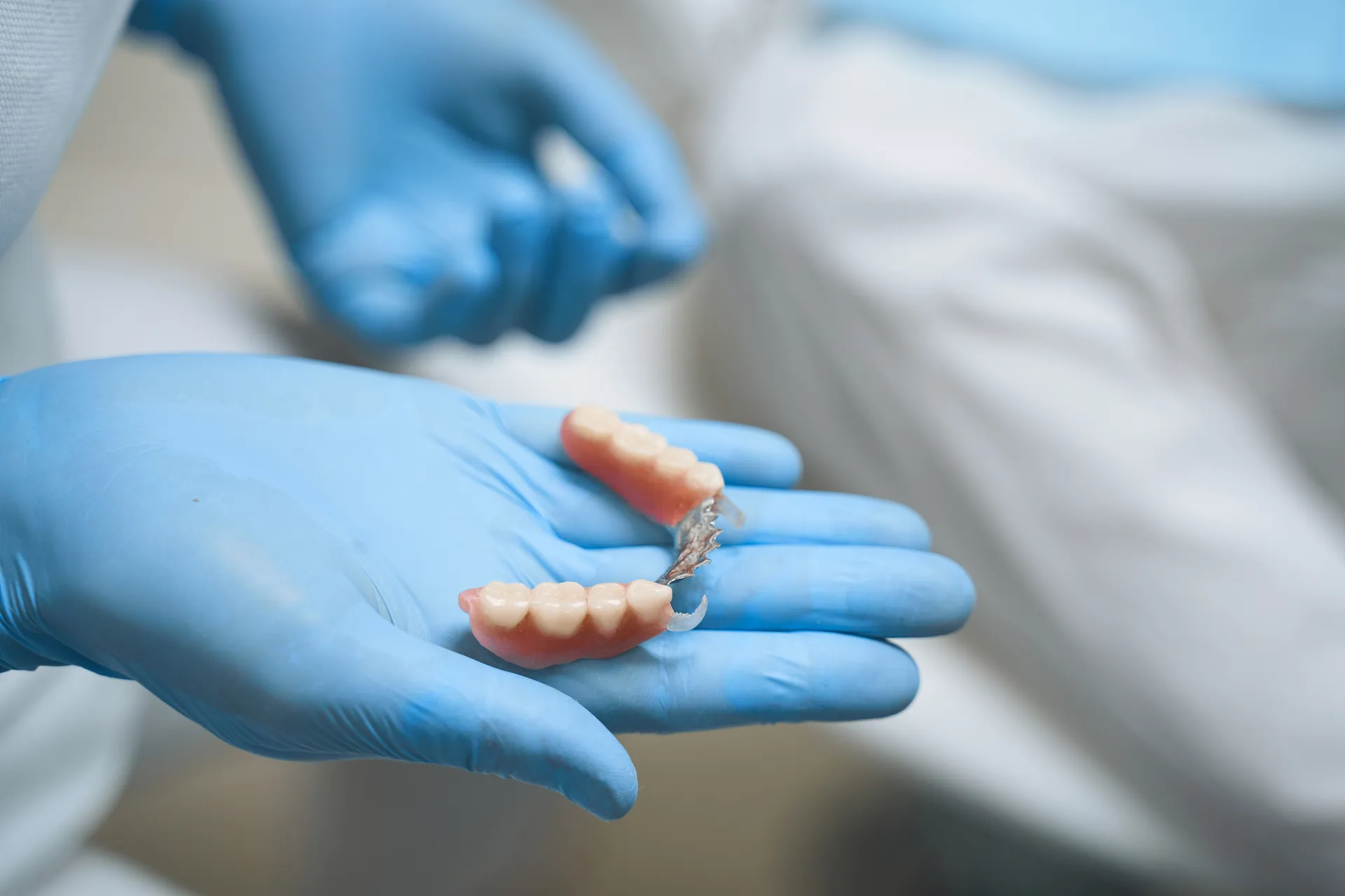 A dentist in blue gloves holding a denture