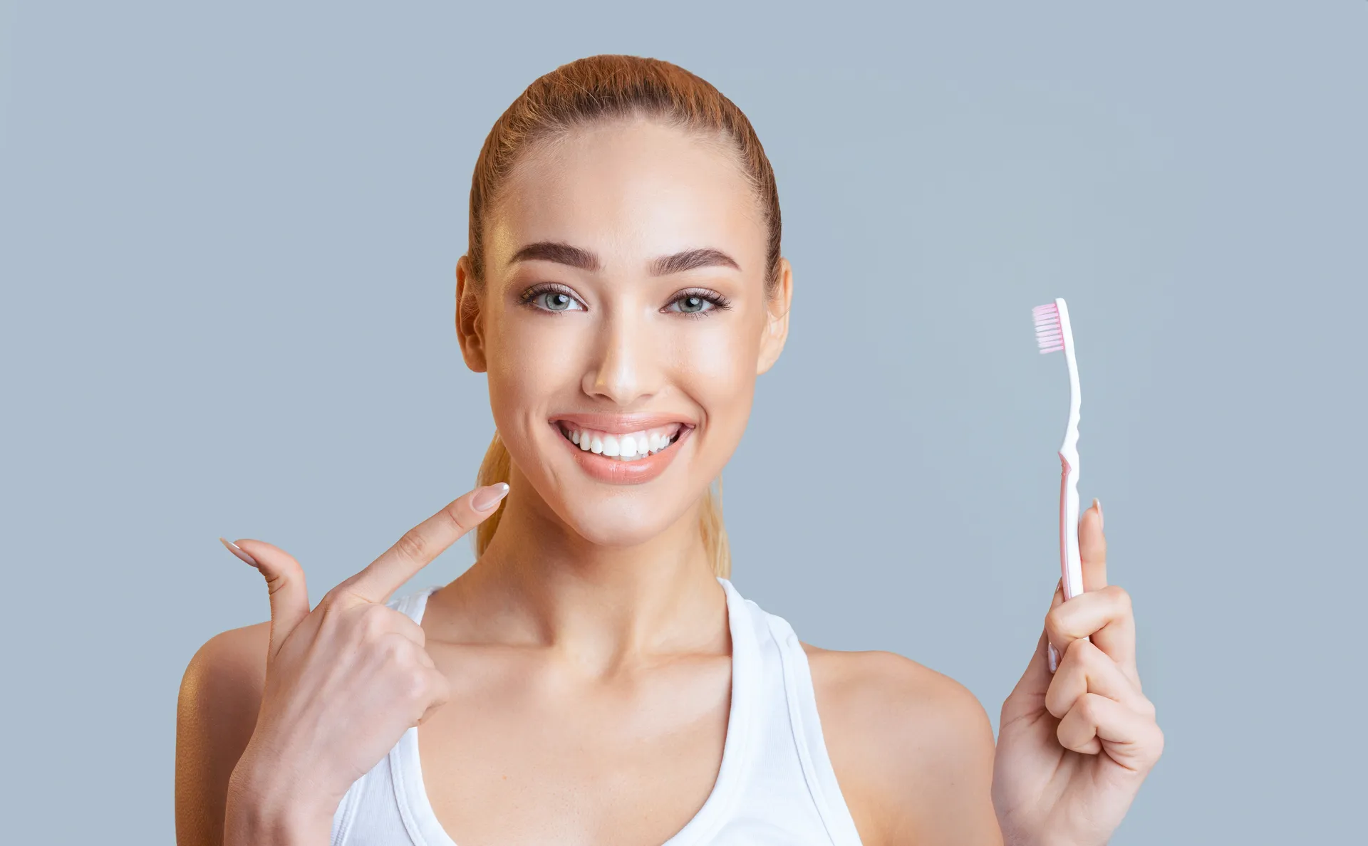 Woman holding a toothbrush and pointing to her smile while talking about home care