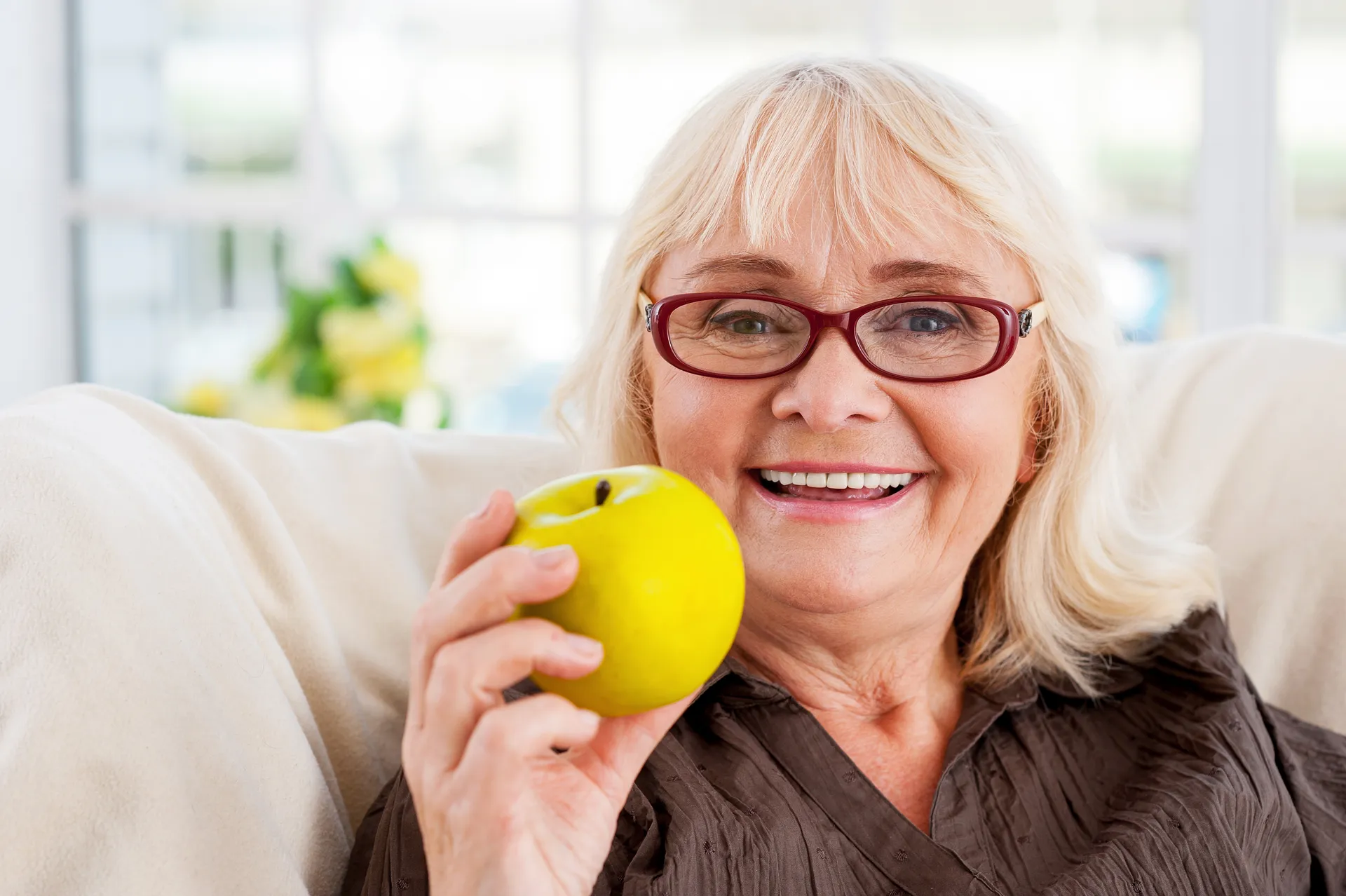 Older woman smiling and holding a yellow apple
