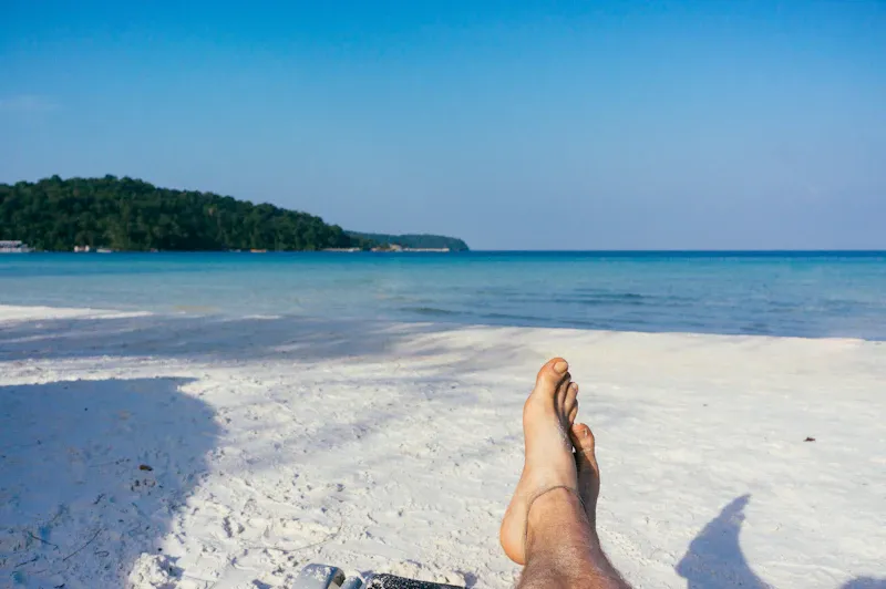 Person lying on the sand with their feet towards the sea