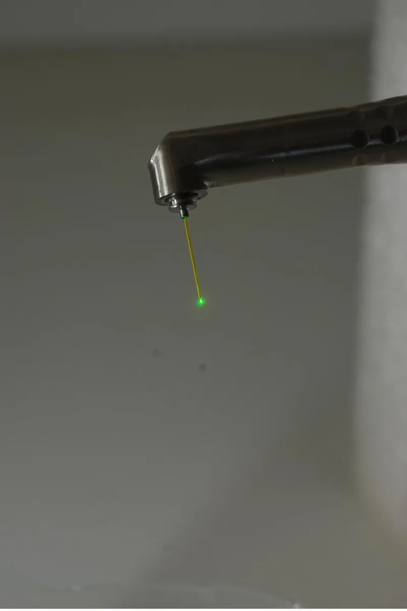A dental laser handpiece and its green guide light, seen from further back