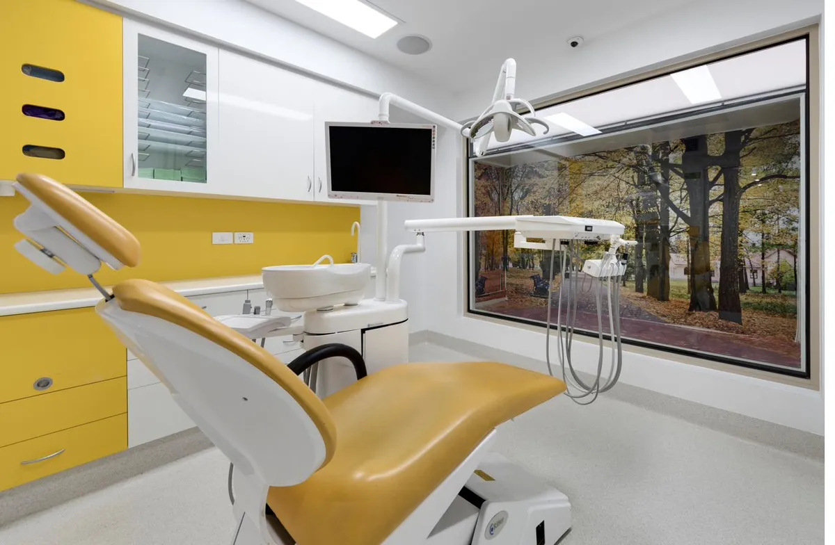 A bright dental treatment room with autumn trees outside the window