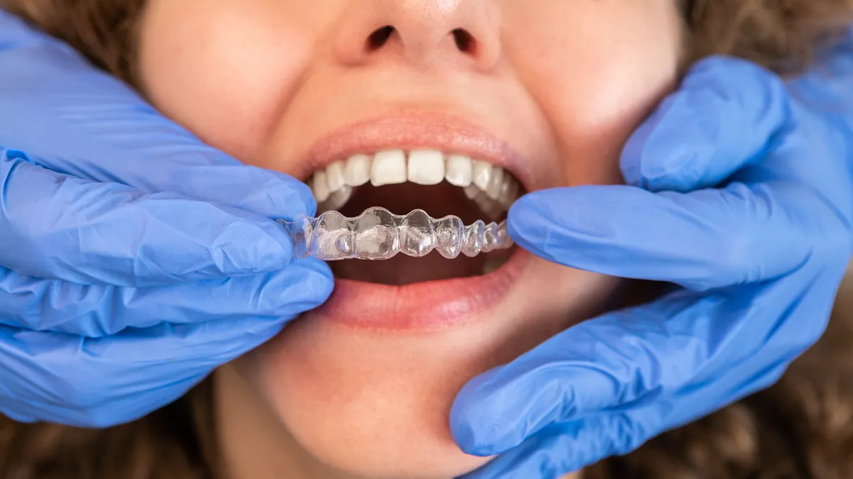 Gloved dentist placing a clear aligner tray on a patient's teeth